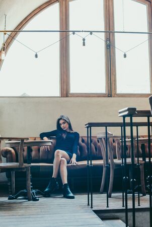 Beautiful elegant brunette girl wearing a black dress is relaxing in a street cafe. Advertising,fashion,commercial design.Girl in a cafe in a black dress brunette.Beautiful girl in a cafe.Tinted photoの写真素材