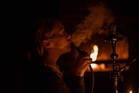Girl. Hookah. Girl smokes a hookah by candlelight. Blonde girl at night by the light of a candle...