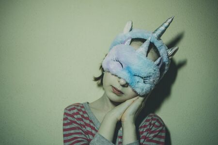 girl with straight hair with a soft white sleeping patch Unicorn on her face. Girl in a unicorn sleep mask. Girl 9 years old. A child in a sleep mask and a hair band on a unicorn. Girl in pajamasの写真素材