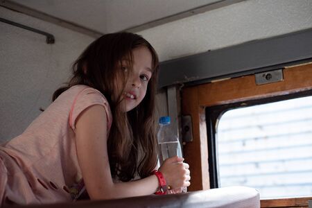 Girl on a train with a bottle of water. girl in a rides in an old train. Nearby is a bottle of water. A 9-year-old girl drinks water in a train from a plastic bottle. Remove thirst. Summer, vacationの写真素材