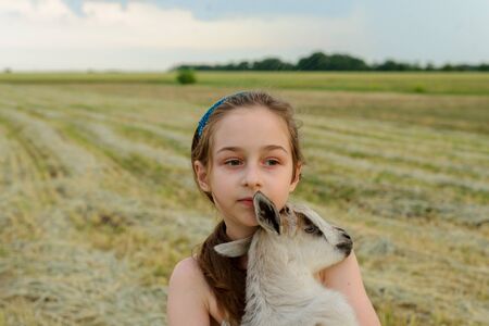 girl with baby goat on farm outdoors. Love and care. Village animals. happy child hugs goat, concept...