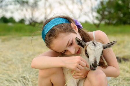 girl with baby goat on farm outdoors. Love and care. Village animals. happy child hugs goat, concept of unity of nature and man. Friendship of child and animals. Happy childhood. Girl and goatの写真素材