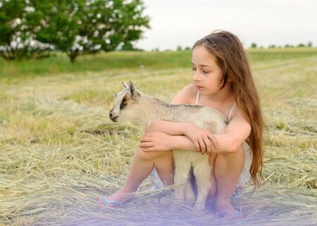 girl with baby goat on farm outdoors. Love and care. Village animals. happy child hugs goat, concept of unity of nature and man. Friendship of child and animals. Happy childhood. Girl and goatの写真素材