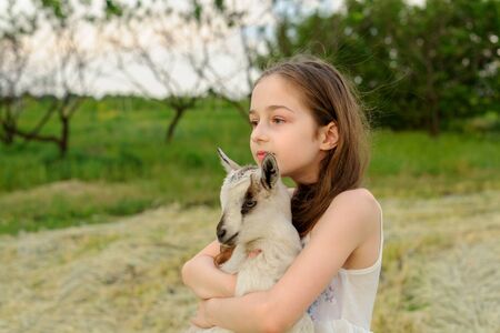 girl with baby goat on farm outdoors. Love and care. Village animals. happy child hugs goat, concept of unity of nature and man. Friendship of child and animals. Happy childhood. Girl and goatの写真素材