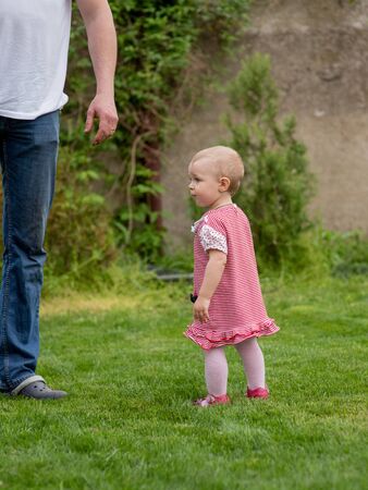 Little child 1 year old baby girl goes. The father walks with the child through the green grass. Baby learns to walk with the support of a parent. 1 year old girl and dad. Life style photo. Familyの写真素材