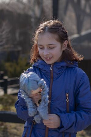 Girl and doll on the street. toddler girl with doll. a walk. A girl of 9 years old plays with a doll on the street. portrait. The girl and the dollの写真素材