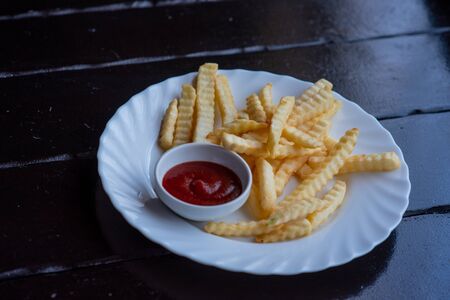 French fries on wooden Table with catchup. French fries and sauce on a white plate on a wooden table