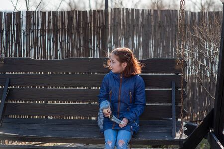 Girl and doll on the street. toddler girl with doll. a walk. A girl of 9 years old plays with a doll on the street. portrait. The girl and the doll. Schoolgirl, spring, 10 years old. Girl with a quadsの写真素材