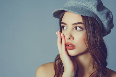 Glamorous young woman wears fashionable dress posing with fluttering hair at grey wall. Girl put forward hand in a black dress and a gray cap. Beautiful young girl with brown curly hairs. portraitの写真素材