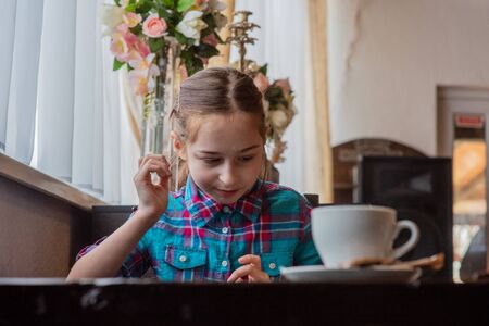 girl eating french-fries. Girl eating french fries in a cafe. A girl of 9 years old has lunch with french fries. French fries, sauce, lunch, food. A schoolgirl is eating and looking at a smartphone.の写真素材