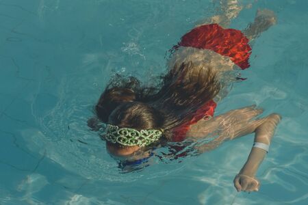 Cute girl with goggles in swimming pool. Girl swims in the pool with goggles. Summer, pool, relaxation, water park, relaxation area. The baby is swimming. Hello summer. Hooray, holidays. healthの写真素材