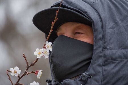 A man wearing a black respiratory mask on his face. A man in the street in a black mask. Virus. Coronavirus. A guy in the spring on the street in a respiratory mask to protect against infection virusの写真素材