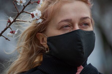 Beautiful young woman in spring clothes on the street with a medical face mask on. Closeup of a...