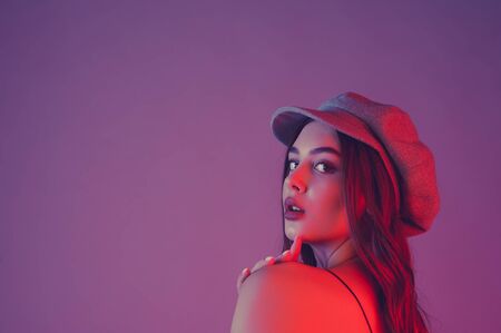 Glamorous young woman wears fashionable dress posing with fluttering hair. Girl in a black dress and a gray cap. girl with brown curly hairs. portrait. beautiful, stylish woman on a pink backgroundの写真素材