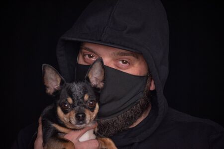 Coronavirus.Man in protective surgical mask.Coronavirus disease COVID-19 is dangerous for pets.Masked man with a dog. Chihuahua and a masked man. Health, bacteria, protection.Guy on a black backgroundの写真素材