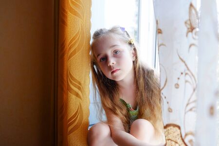Little girl by the window. A 5 year old girl sits by the window at home. Childhood, child, window. Stay at homeの写真素材