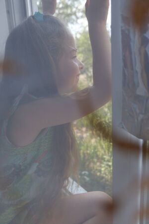 Little girl by the window. A 5 year old girl sits by the window at home. Childhood, child, window. Stay at homeの写真素材