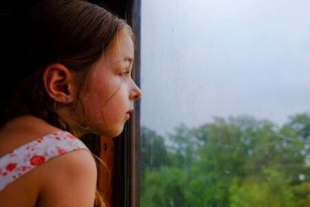 Cute girl in the train. Summer Vacation and Travel Concept. A girl of 5 or 6 years old rides on a train. Teen travels. Little girl with long hair. Child portraitの写真素材