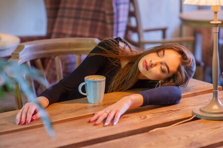 Portrait of a girl. Brunette in a coffee shop. elegant lady in a black dress, in a restaurant alone. Girl in a cafeの写真素材