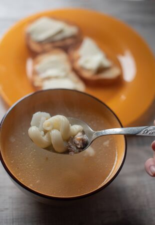 Chicken soup with pasta on the table. Pasta soup and bread and butterの写真素材