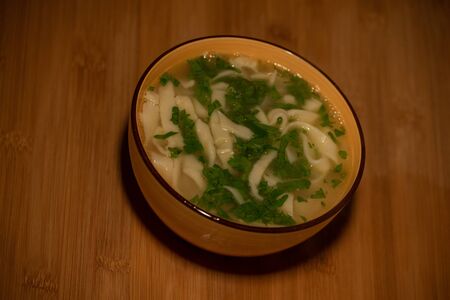 Chicken Noodle Soup. Chicken and noodle soup on an orange tablecloth in an orange plate. Food photography. Hot dish. Broth with noodles. Chicken, noodles. Homemade noodles and broth. Dill and parsleyの写真素材