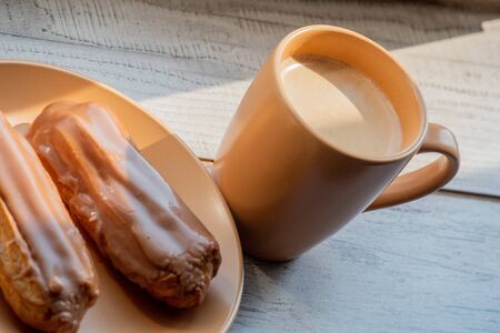 Custard cakes with cream. Custard cakes poured on top with brown and white sugar icing. Sweet treats for tea or coffee. Close-up. Selective focus. Custard cake. Dessert. Four cakes on a beige plateの写真素材