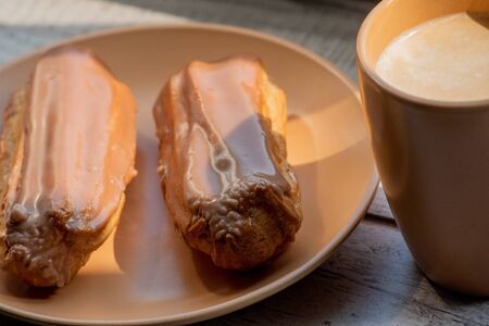 Custard cakes with cream. Custard cakes poured on top with brown and white sugar icing. Sweet treats for tea or coffee. Close-up. Selective focus. Custard cake. Dessert. Four cakes on a beige plateの写真素材