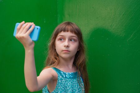 Cute little girl using smartphone on green background. Little girl takes a selfie. Alpha Generation Millennial Children - Active Internet Users. generation Z.の写真素材