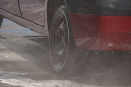 red car during washing process. transport in foam at a car wash. Manual car wash with pressurized water in car wash outside. Summer Washing. Cleaning Using High Pressure Water.の写真素材