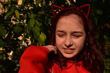 Cute teenage girl 8-9 years old wearing trendy hipster clothes posing. Teenager girl in a red jacket on a background of greenery, at sunset.の写真素材