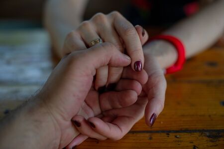 Closeup on two young lovers holding hands at a table. Male and female hand in hand. Love and family...