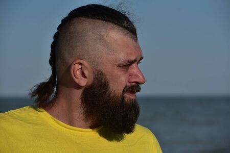 A young man wearing a yellow T-shirt and shorts walking along the sandy beach. Man in a yellow T-shirt with a beard on the background of the sea. Man and sea. Sea vacation summer concept. Portrait of a 40 years old man with a beardの写真素材