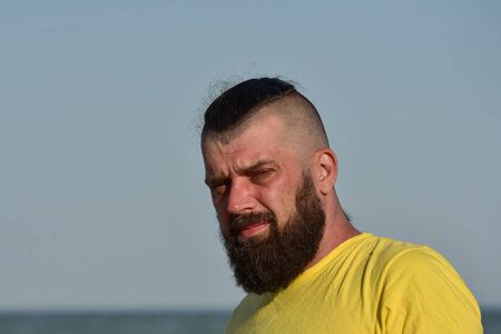 A young man wearing a yellow T-shirt and shorts walking along the sandy beach. Man in a yellow T-shirt with a beard on the background of the sea. Man and sea. Sea vacation summer concept.の写真素材