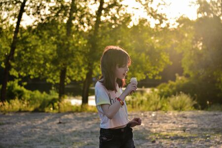 Beautiful little girl eats ice-cream in the summer. girl eating ice cream. 9 years old girl walking in the parkの写真素材