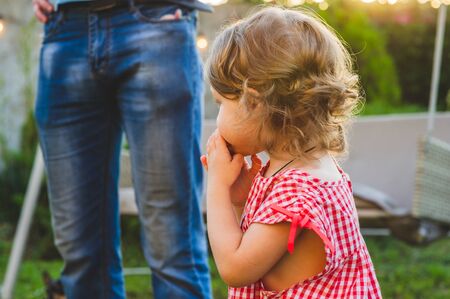Girl Eating Sausage At Family Barbeque. 2 years old girl eats sausage. Little girl on nature mouth a piece of sausage. A child on a walk. Portet baby girl 2 years old.の写真素材