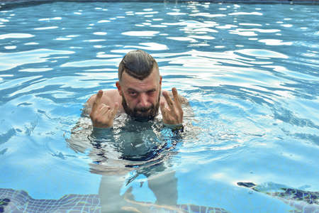 Bearded man swimming in a pool. Man with a beard in the pool. Brunette man on vacation. Summer...