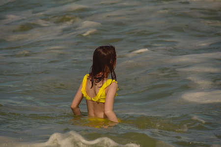 Girl at sea. The portrait of the young girl. Teenager summer vacation sand. Sunny day and the sea. Childhood travel vacation. Teenager in a yellow swimsuit on the beach. Teenager swims in the seaの写真素材