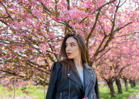 Young beautiful girl with long hair enjoys the beauty of spring nature near the blossoming sakura...