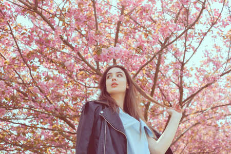 Young beautiful girl with long hair enjoys the beauty of spring nature near the blossoming sakura...