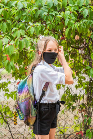 Schoolgirl girl in a black protective mask with a backpack. Schoolgirl in a white shirt and black shorts, school uniform. Fall. Back to school soon.の写真素材