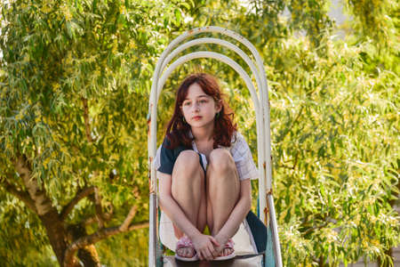 Outdoors portrait of beautiful young brunette girl. The girl slides down the children's slide. Teenager 9 or 10 years old in summerの写真素材