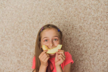 Portrait of girl biting melon. Girl eating melon. Teenager in pink t-shirt at home. Healthy food, vitaminsの写真素材