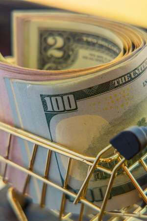 Supermarket grocery push cart for shopping with bundle of dollars money banknote cash. Dollars in...