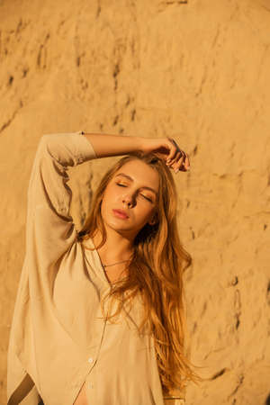 Girl on the background of sands and sky. Girl in a beige shirt and sands. Portrait of a girl