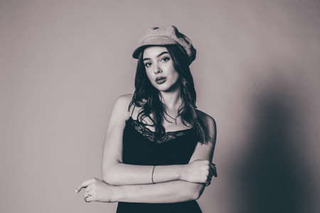 Glamorous young woman wears fashionable dress posing with fluttering hair at grey wall. Beautiful young girl with brown hairs. Portrait, black and white photography of a girl in the studioの写真素材