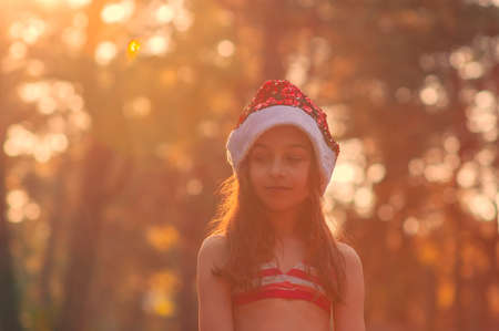A child is playing with a santa claus hat. Happy little girl in Santa Claus hat outdoors in summer.Concept New Year or Christmas series of photos.Little girl in a Santa Claus hat by the poolの写真素材