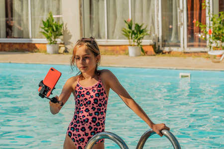 Vacation and technology. Colorful portrait of pretty young girl taking selfie portrait near swimming...