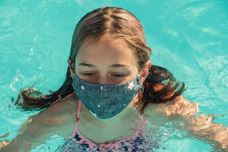 Girl child in a medical mask and swimsuit near the pool, the concept of rest and vacation during the...