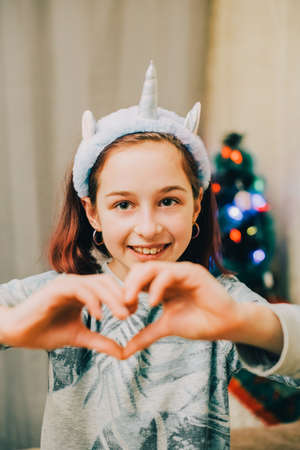 close up Portrait of 9 or 10 Years Old beautiful girl. Studio shot of adorable little 9 year old girl. Happy young kid posing over Gray background. Young model. Girl showing hands with her heartの写真素材
