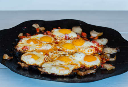 Eggs are fried on a fire in the street. Fried eggs with bacon. A dish of many fried eggs on a...